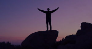 Silhouette of person with out stretched arms standing on a rock at dusk